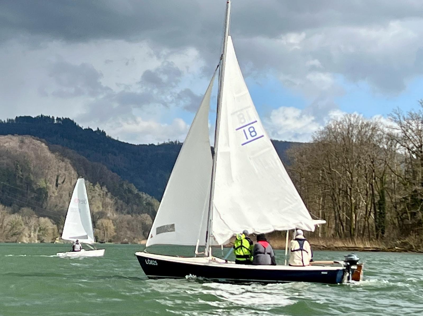 Segelboot mit mehreren Leuten auf dem Wasser, kleines Segelboot im Hintergrund